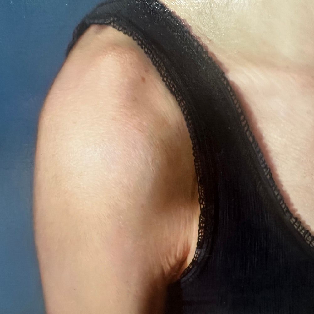 Macro photograph of a painted shoulder and the lace edge of a black top against a blue ground