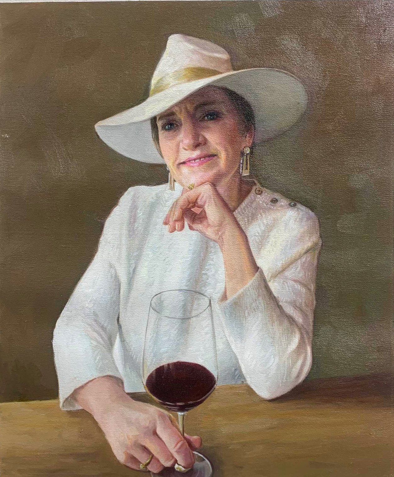 A woman in a white hat and pale jacket seated with a glass of red wine.