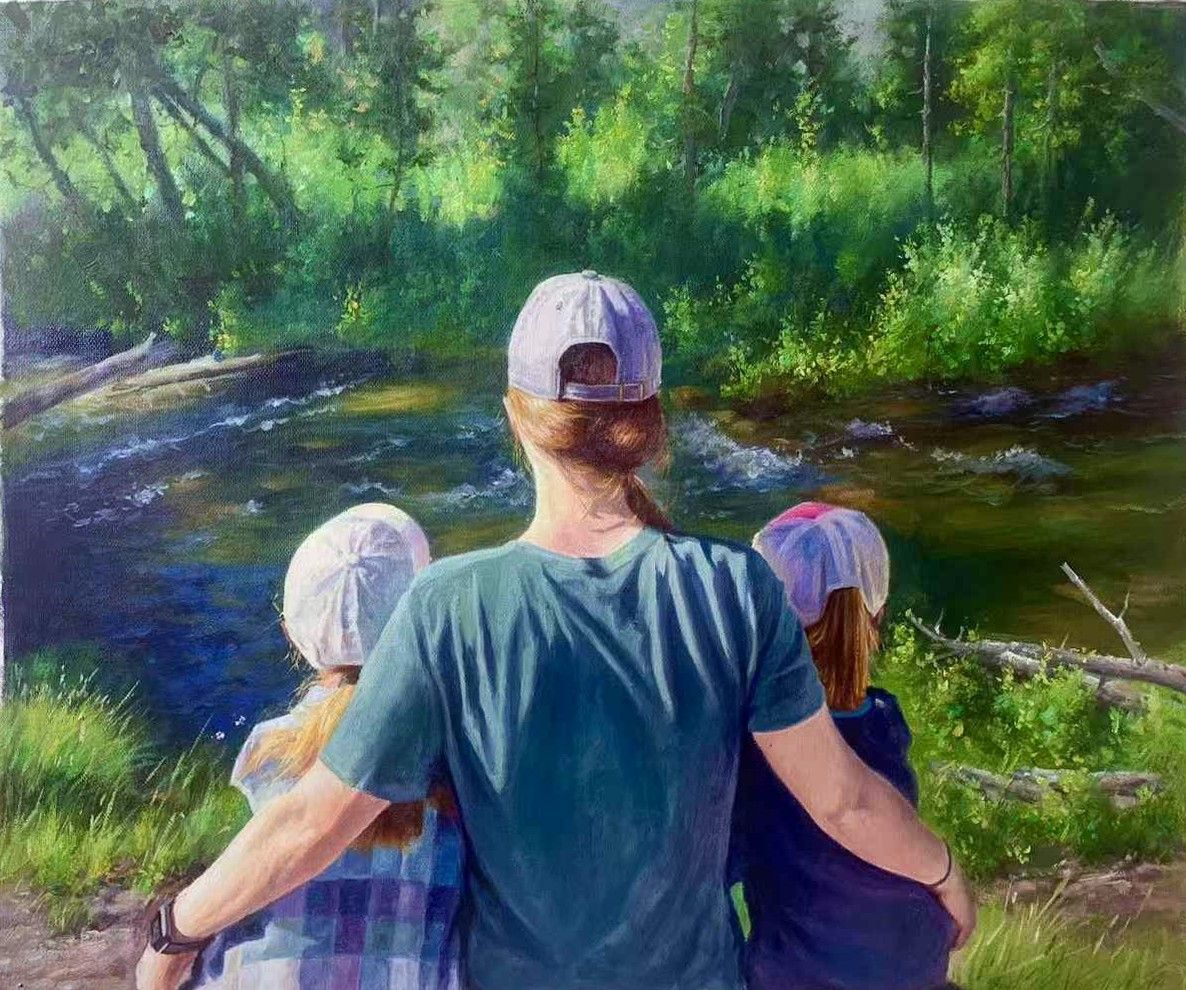 A mother with two children seen from behind beside a wooded river.