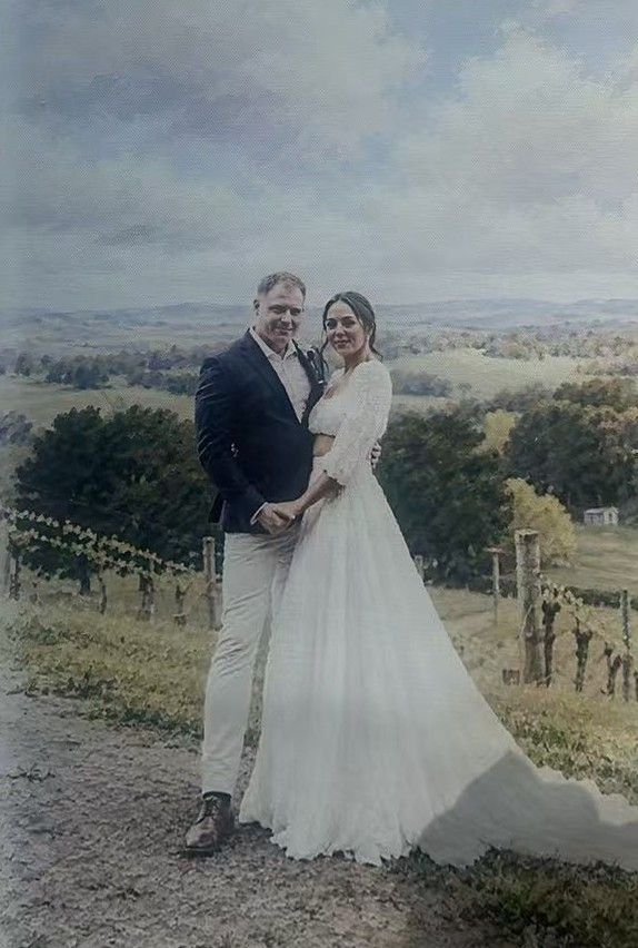 A bride and groom standing in a countryside landscape.